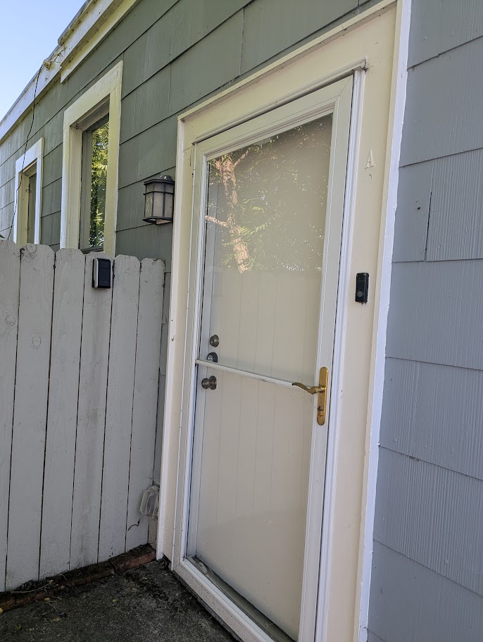 Front entry door of Unit A — brass hardware, weathered trim, storm door in decent shape